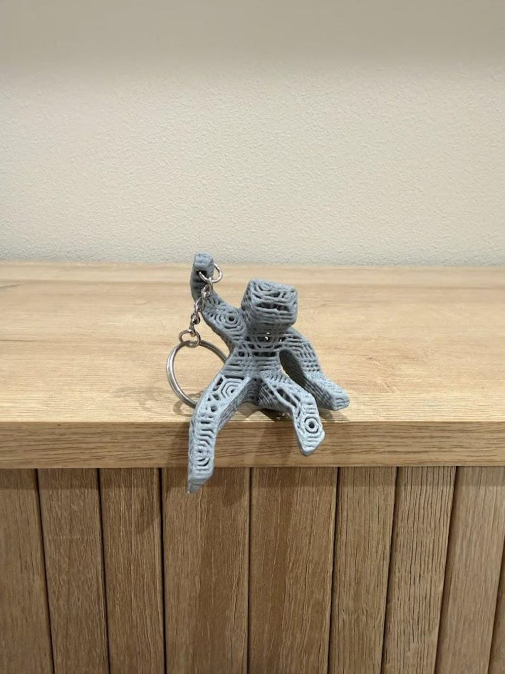 3D-printed alien keychain on a wooden surface with a neutral background