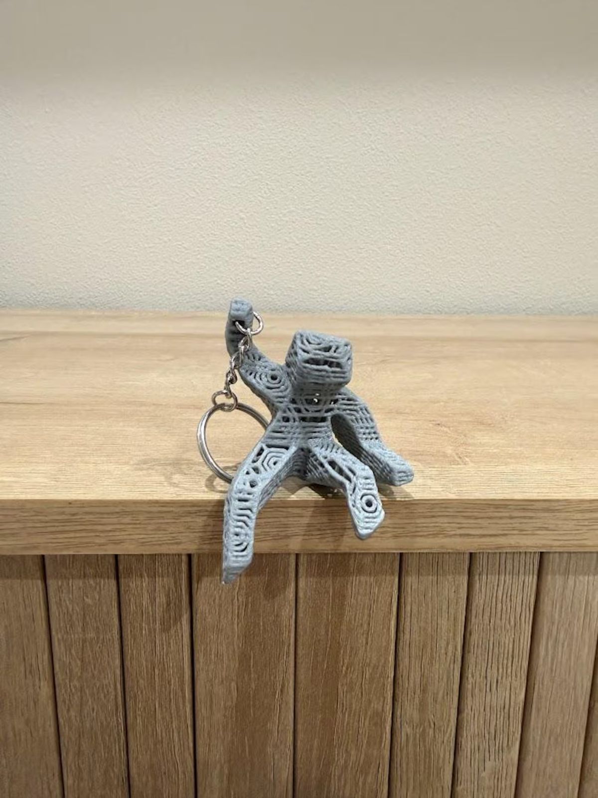 3D-printed alien keychain on a wooden surface with a neutral background